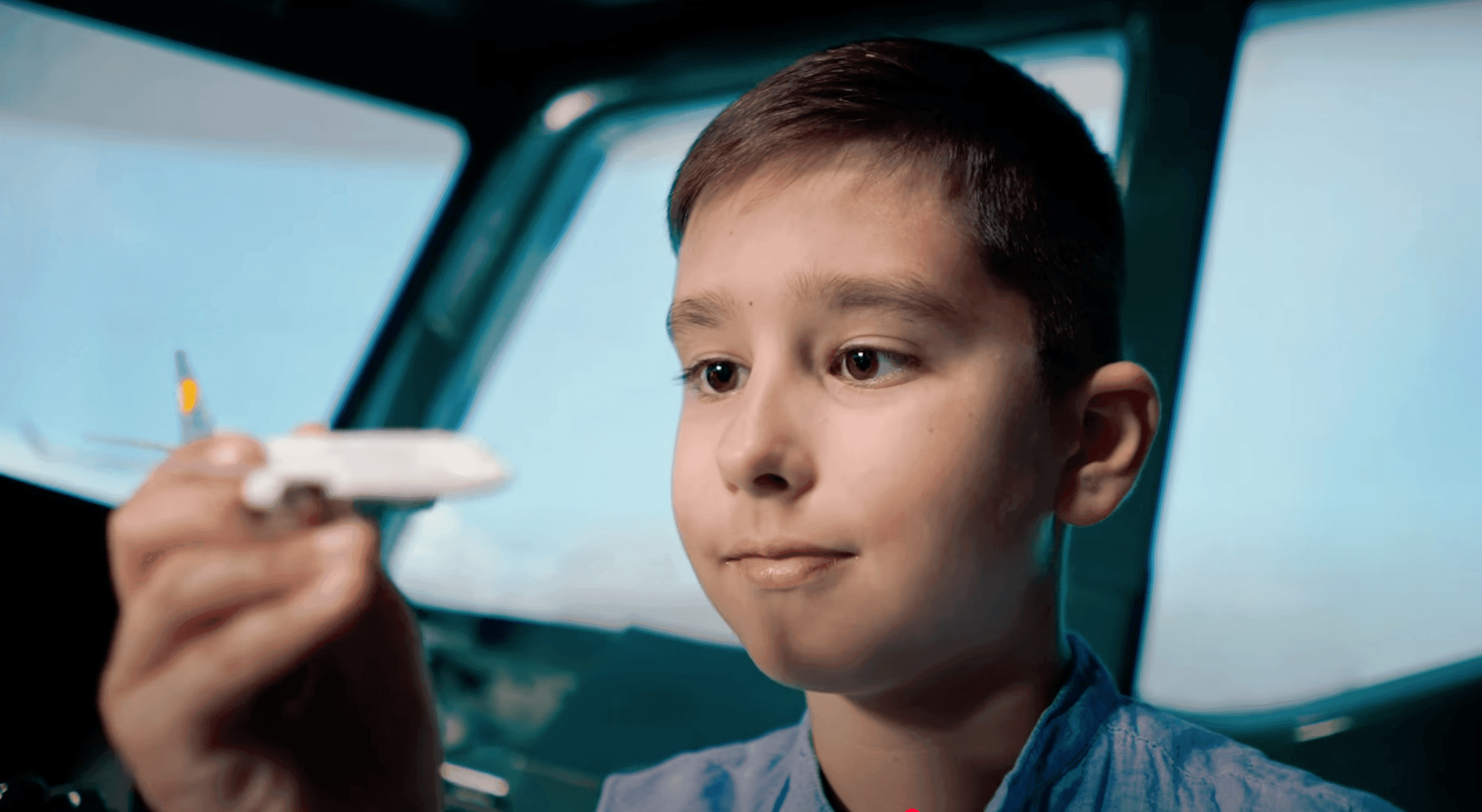 A young boy holding a toy airplane inside a WeFly flight simulator cockpit, dreaming of becoming a pilot.